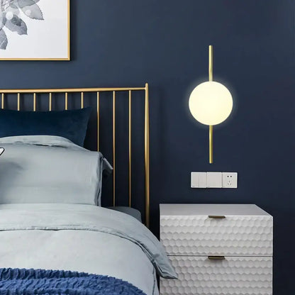 Minimalist gold wall light with frosted white globe shade and slender gold arm sconce light for bedroom use