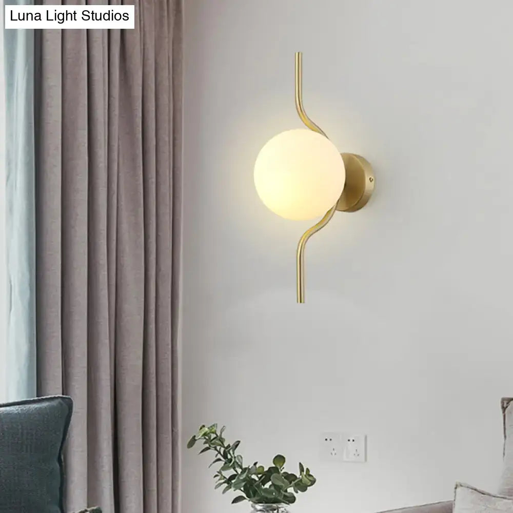Minimalist gold wall light with a gold arm, curved metallic sconce light, and frosted white globe shade for bedroom use