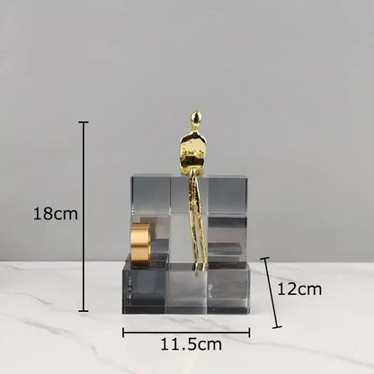 Gold-colored abstract decorbites golden thinker perched on a transparent thinker crystal base with geometric cube design