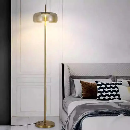 Gold-finished floor lamp with sleek cylindrical gray glass floor shade emitting warm light for living room use