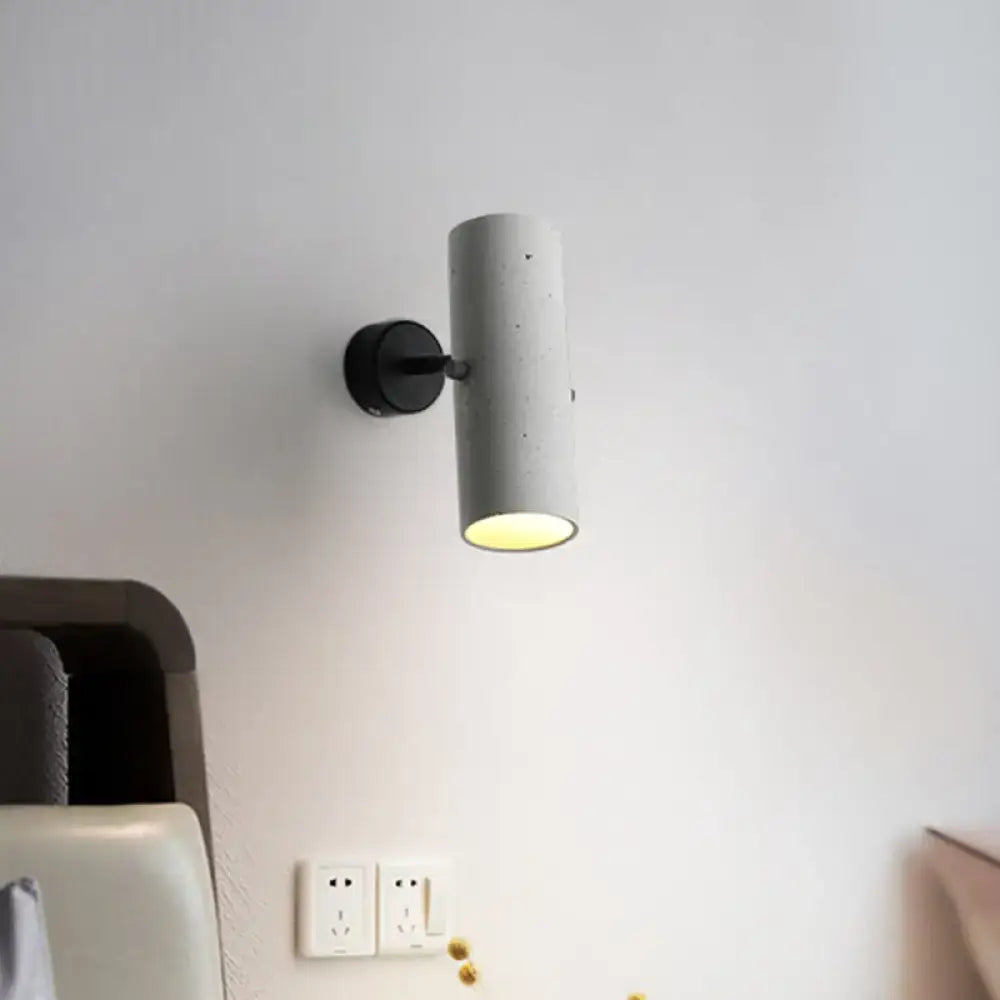 Minimalist grey led wall spotlight with cylindrical matte finish and black bracket emitting warm bedroom light