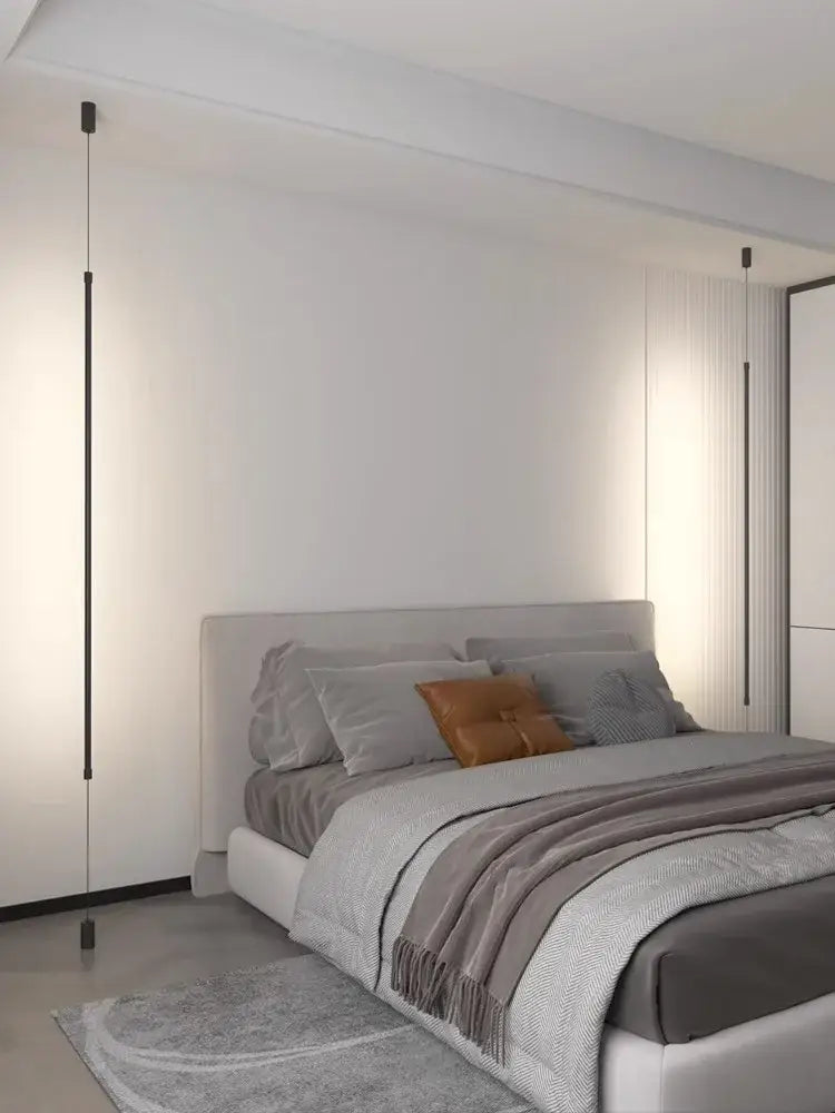 Modern gray upholstered bed with tufted headboard and layered bedding illuminated by minimalist matte black bedside pendant light straight strip