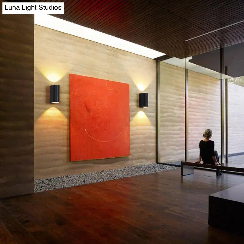 Minimalist matte black tube wall light outdoor sconce mounted on textured wall with vibrant orange abstract canvas painting