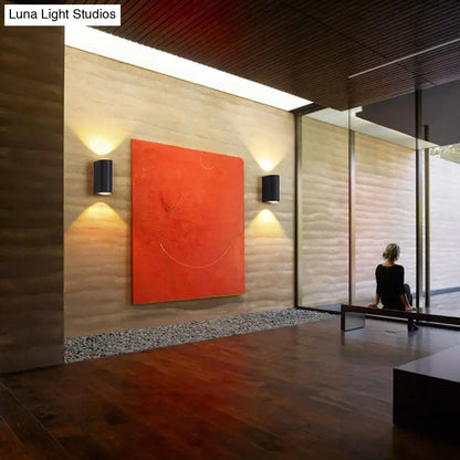 Minimalist matte black tube wall light outdoor sconce mounted on textured wall with vibrant orange abstract canvas painting