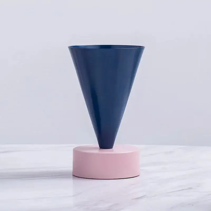 A sleek navy blue geometric triangle vase with matte finish resting on a soft pink base for decorbites decor