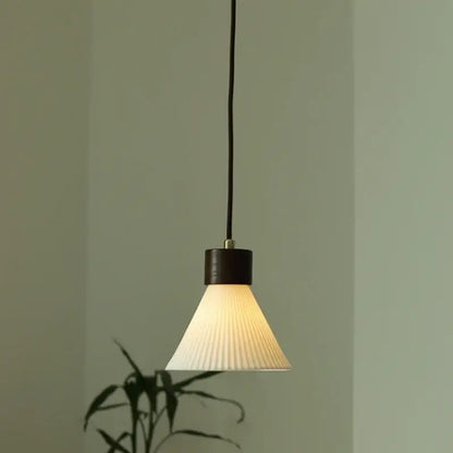 Minimalist pleated glass and wood pendant light fixture with off-white shade and dark wood top for kitchen use