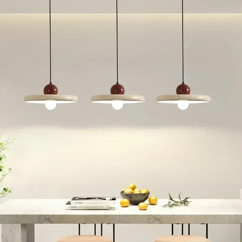 Three modern pendant lights with matte white ceramic discs and glossy burgundy tops in a minimalist cord pendant design