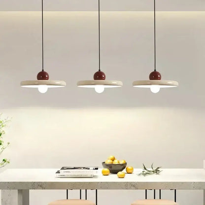 Three modern pendant lights with matte white ceramic discs and glossy burgundy tops in a minimalist cord pendant design