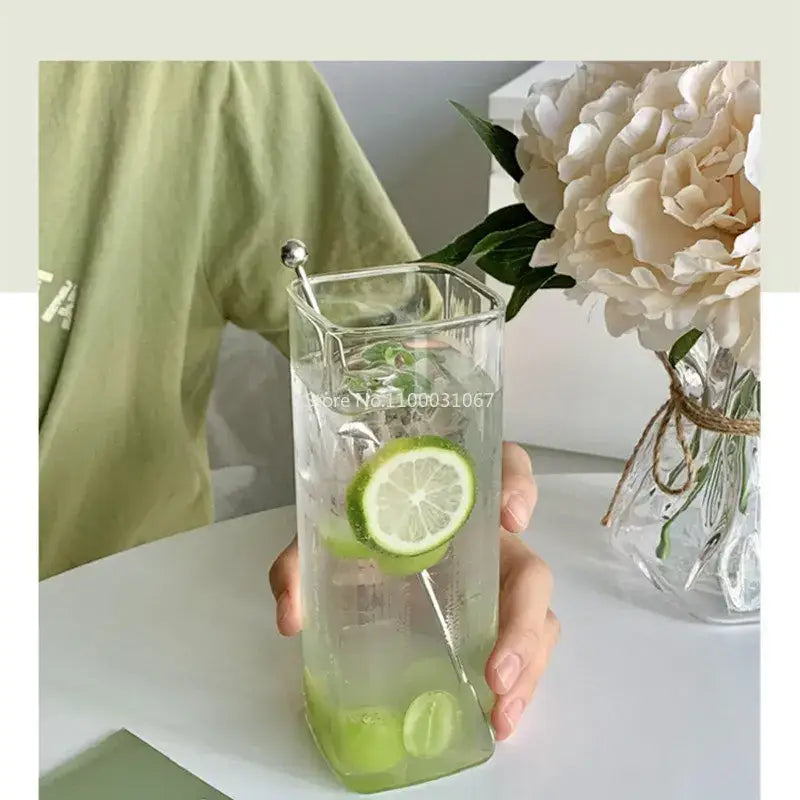 Minimalist clear square glass juice cup filled with ice and lime slices with a silver spoon inside for kitchen use