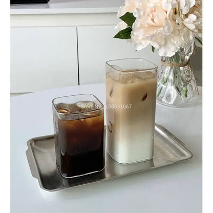Minimalist rectangular glass juice cup filled with iced coffee and milk on a metallic tray for kitchen drinkware