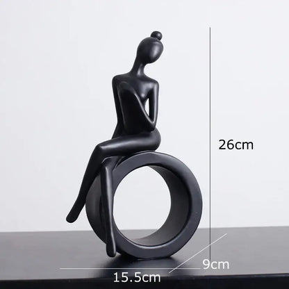 Black matte-finished abstract figures sculpture of a seated woman with hair in a bun on a circular ring base for decor