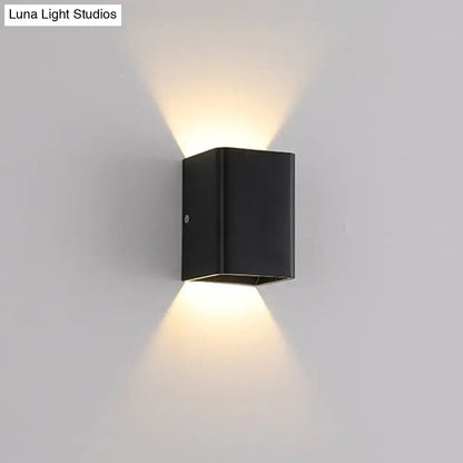 Black rectangular wall lamp with cube shade and brass accents emitting warm light for modern bedroom use