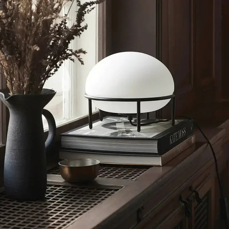 Minimalist white glass ball table lamp with black metal frame on stacked books suitable for bedroom decorbites table lamp