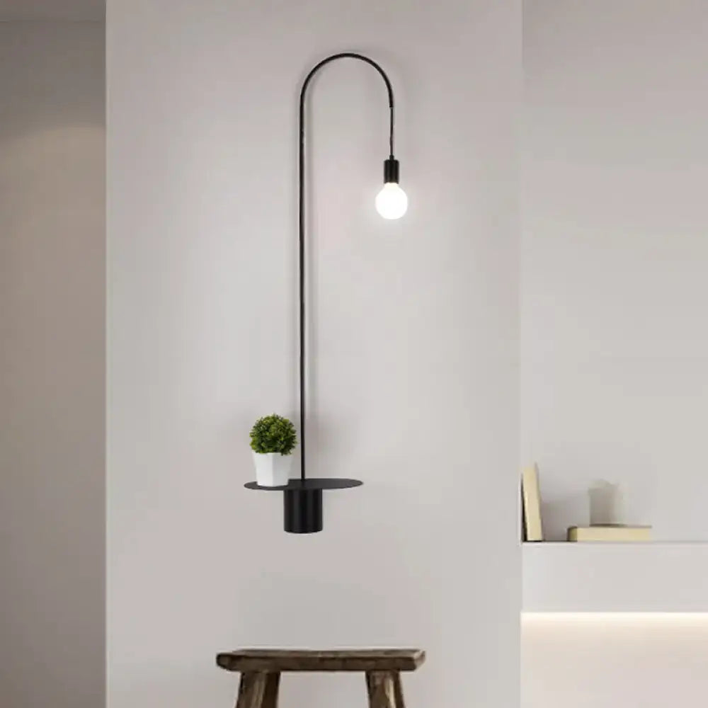Minimalist black metal wall sconce with arched arm single exposed bulb and circular shelf holding white pot greenery wall light