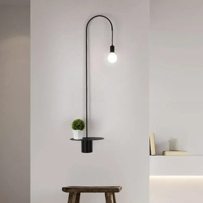 Minimalist black metal wall sconce with arched arm single exposed bulb and circular shelf holding white pot greenery wall light