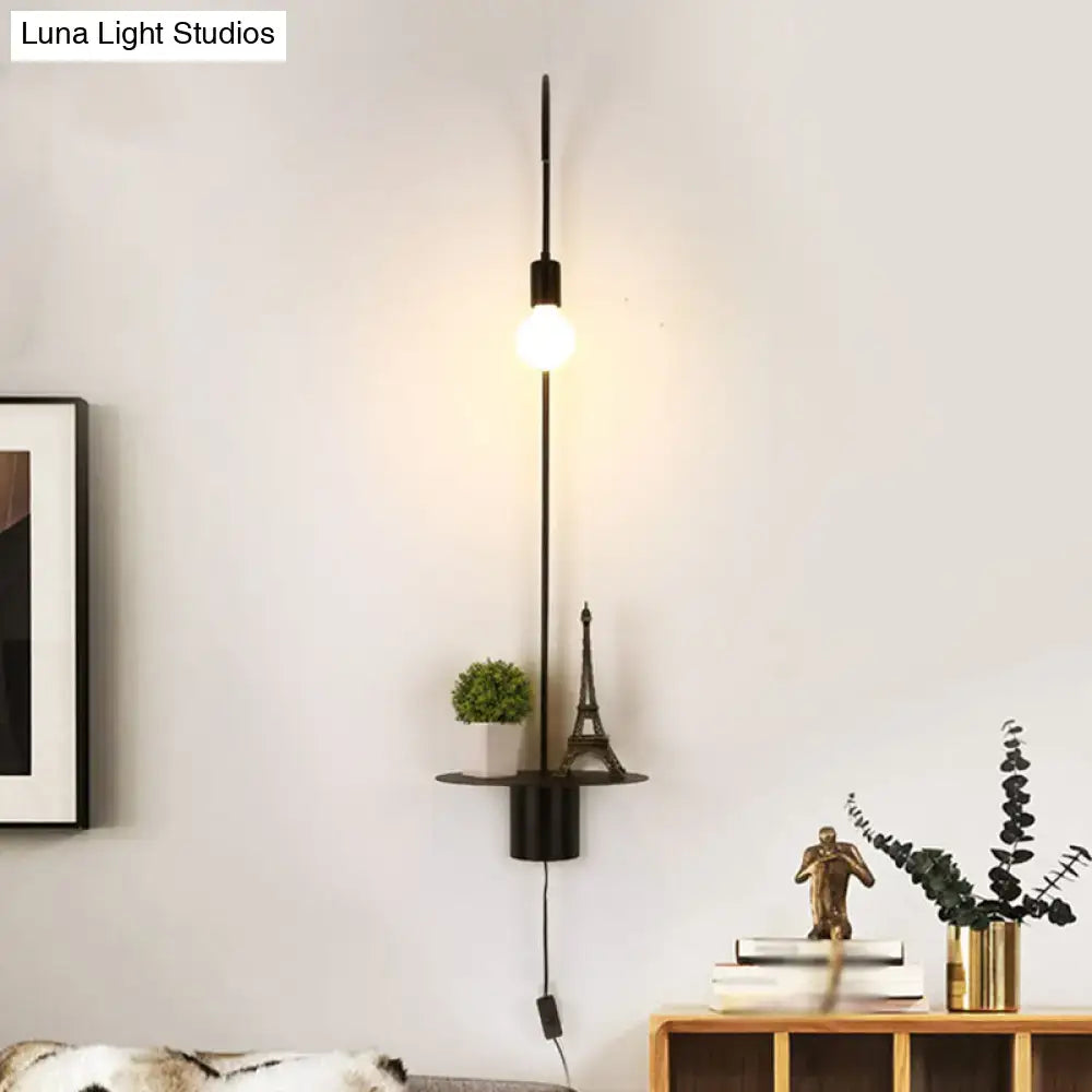 Black metal wall sconce with vertical rod exposed bulb and circular shelf holding plant and miniature eiffel tower wall light
