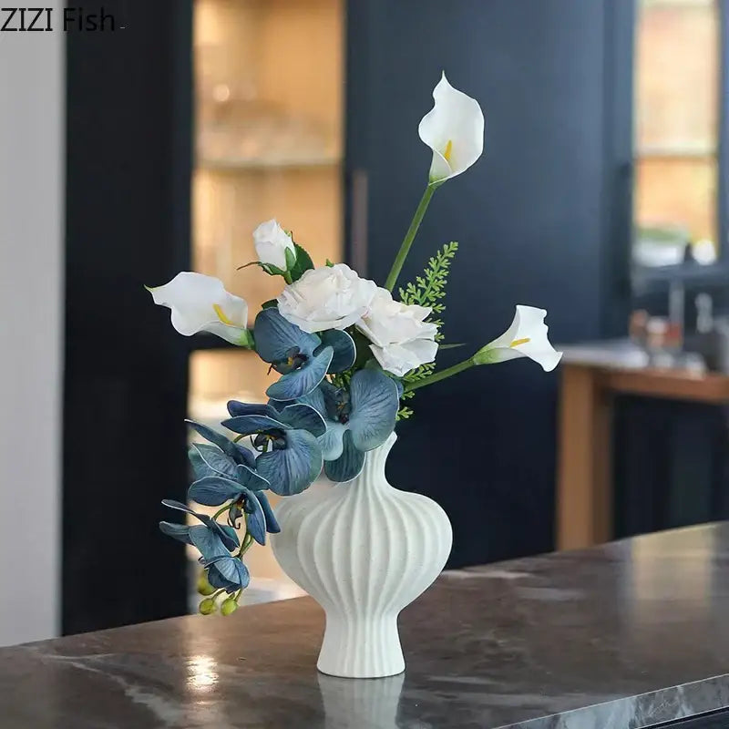 Minimalist white heart shape ceramic vase with vertical ridged texture holding white calla lilies and blue orchids decorbites heart shape decor