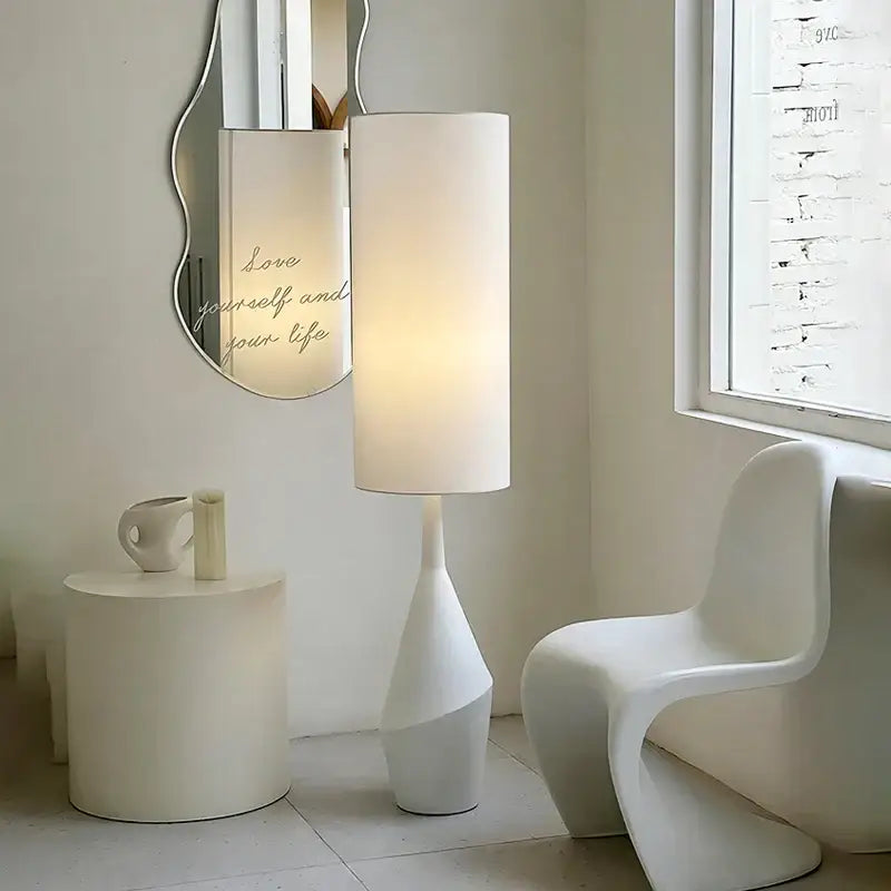 A sleek white led floor lamp with a cylindrical shade and sculpted tapered base for minimalist living rooms