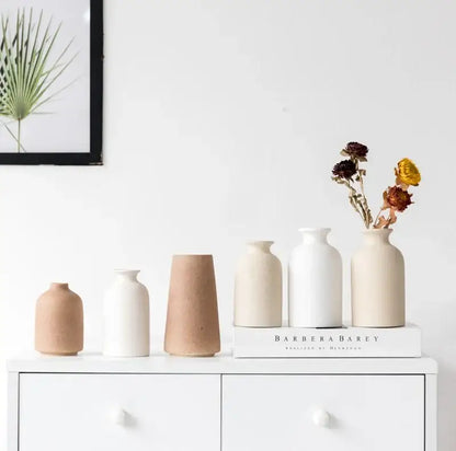 A set of five minimalist decorbites ceramic vases in beige and white with dried flowers on a white surface
