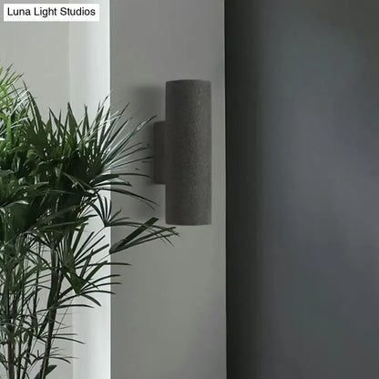 Minimalist gray cylindrical wall sconce with textured concrete finish and compact fixture height for stair lighting
