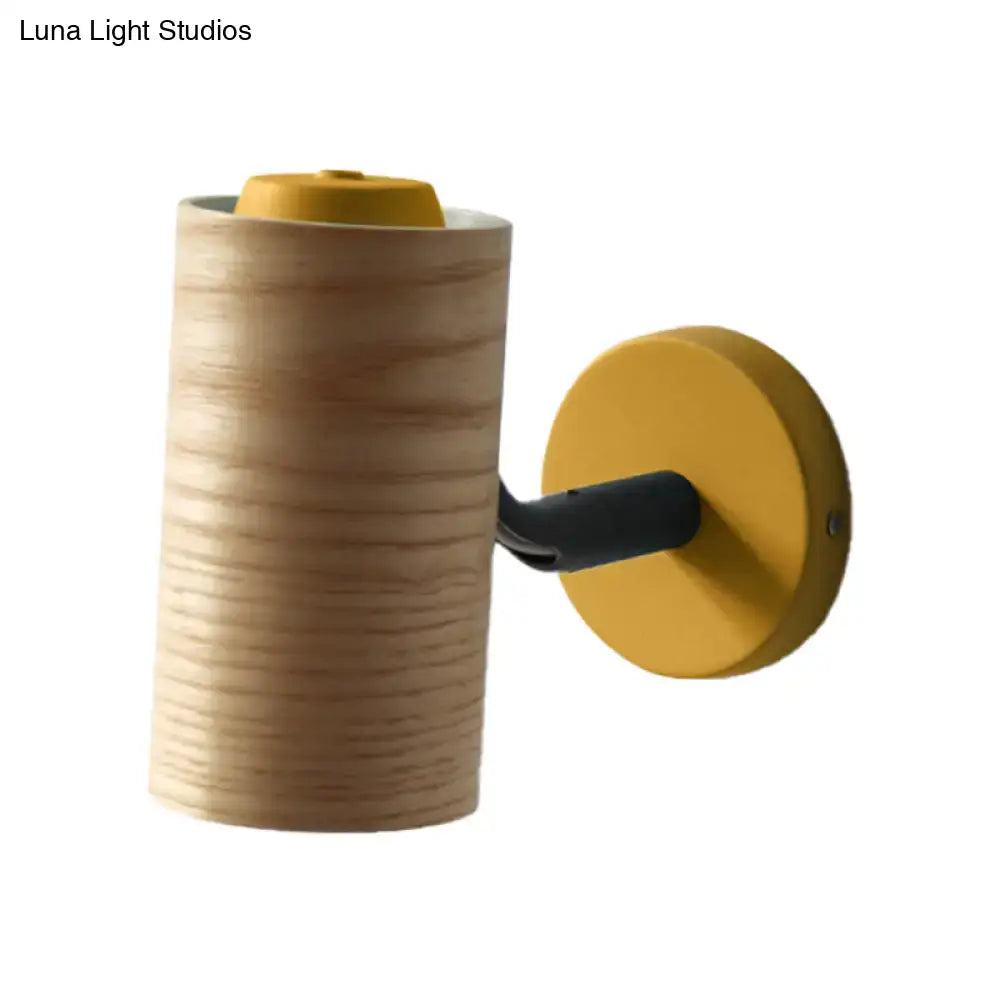 Minimalist wood wall light fixture with cylindrical wooden body, mustard-yellow base, and black arm for bathroom use