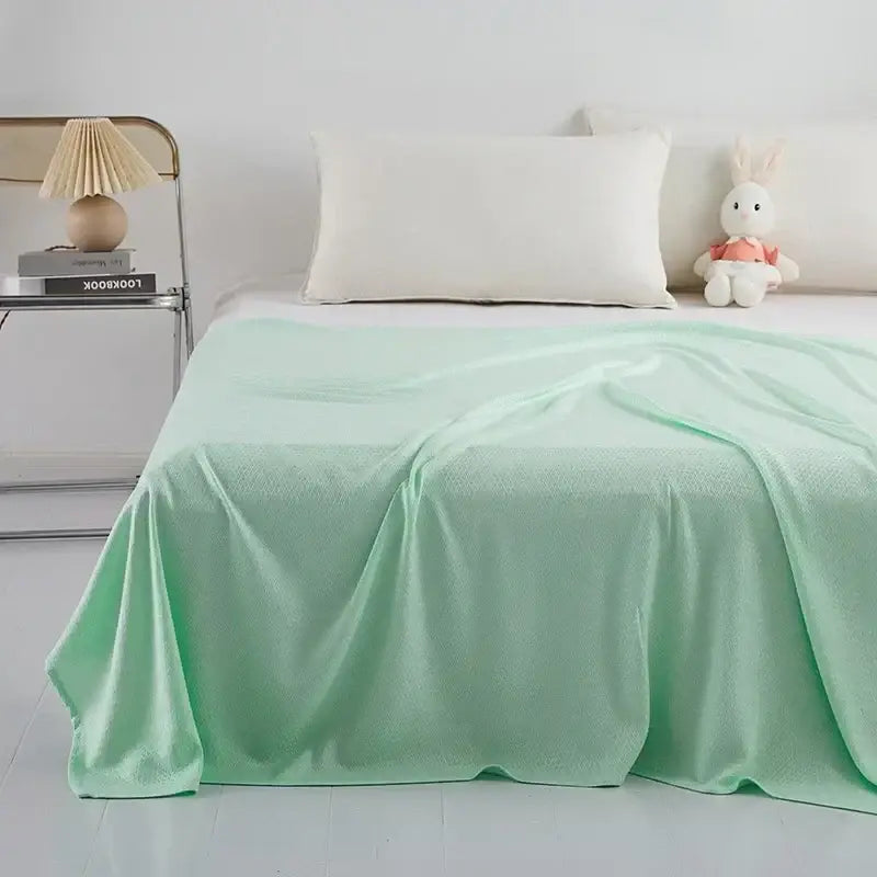 A soft mint green bamboo fiber cooling summer blanket with diamond quilt pattern draped neatly on a bed by decorbites