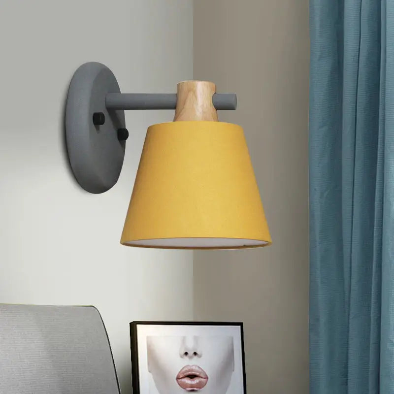 Yellow conical lampshade bucket wall lamp mounted on gray metal arm with natural wood accent for bedroom use