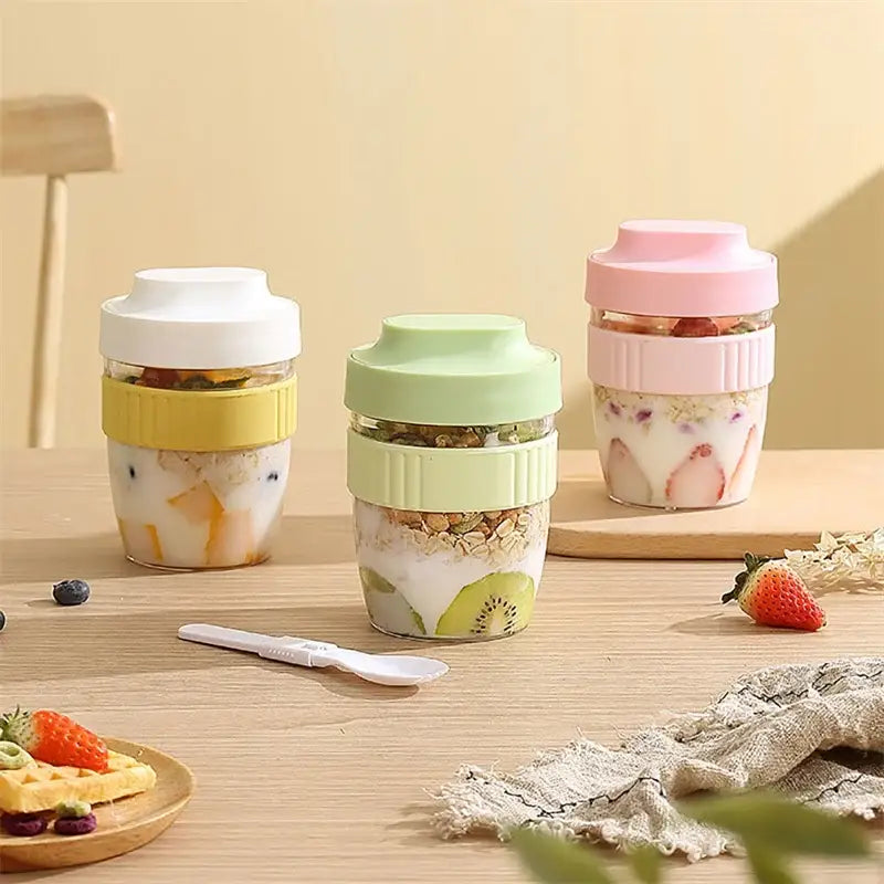 Three colorful translucent plastic decorbites breakfast cups with lids and bands filled with fruit-topped yogurt