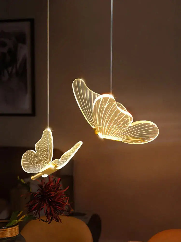 Two elegant modern acrylic butterfly led chandelier pendant lights with translucent wings and glowing golden interiors
