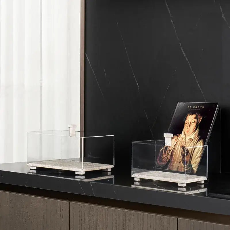 Modern acrylic display case with travertine base holds art books on black countertop for dining room use