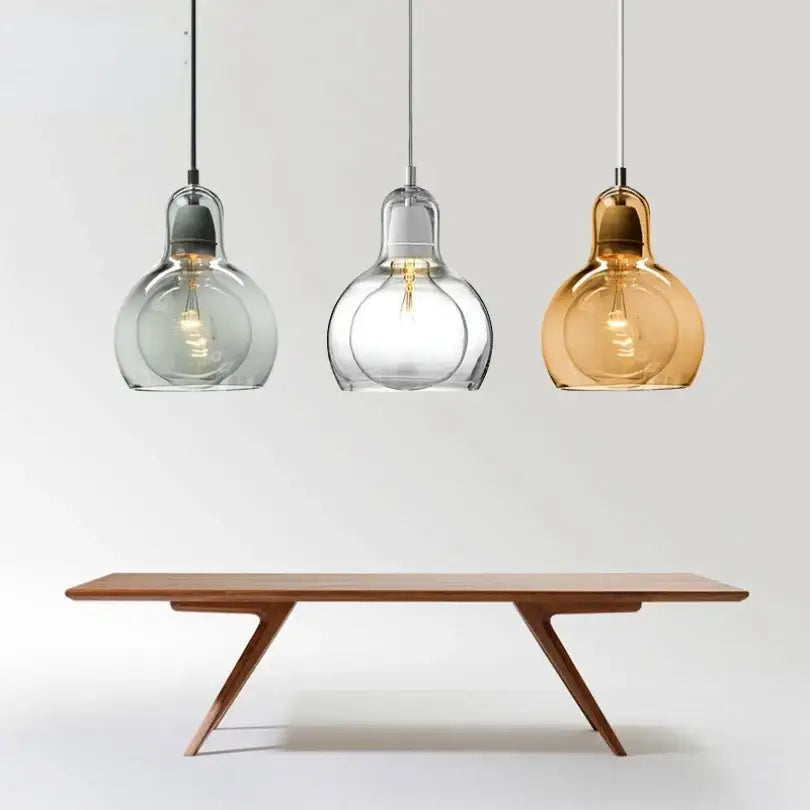 Three modern amber and gray glass pendant lights with bulbous shades hang above a minimalist wooden dining table