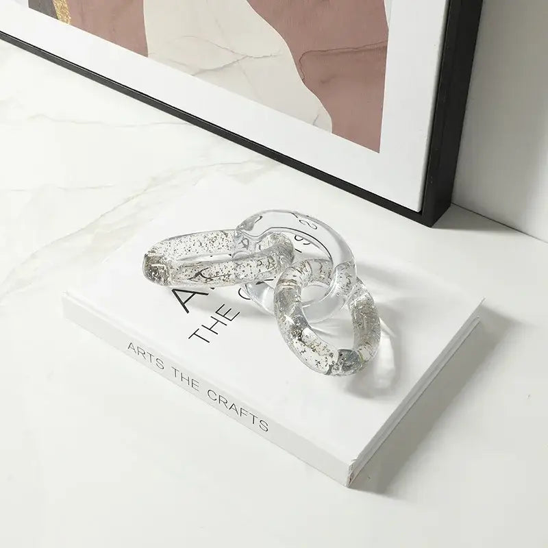 Clear glass chain with embedded silver glitter resting on white book for decorbites colorful geometric ring decor