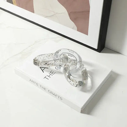 Clear glass chain with embedded silver glitter resting on white book for decorbites colorful geometric ring decor