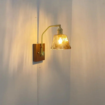 A warm-toned brass wall lamp with textured amber glass copper led shade and wooden mounting plate for bedroom lighting
