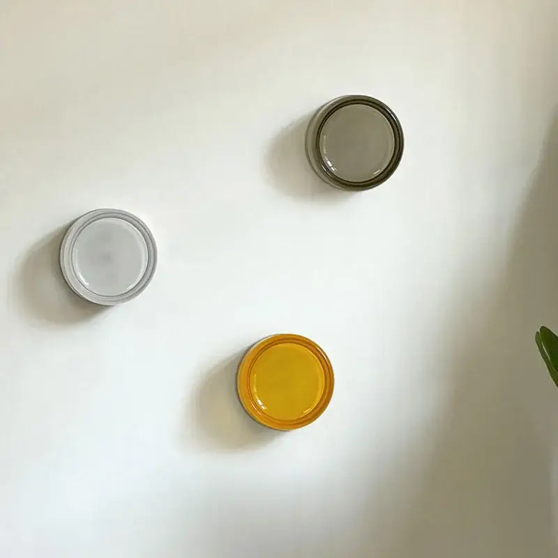Three minimalist circular wall sconce hooks in matte white translucent gray and vibrant yellow for decorbites amber jelly led