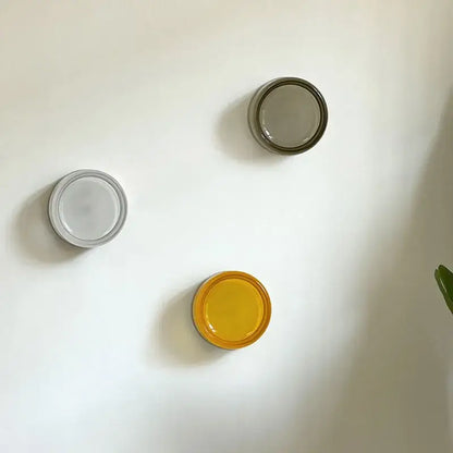 Three minimalist circular wall sconce hooks in matte white translucent gray and vibrant yellow for decorbites amber jelly led