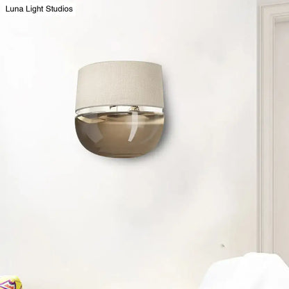 Modern wall sconce with a textured beige fabric shade and a sleek tan glass lower half for bedroom lighting