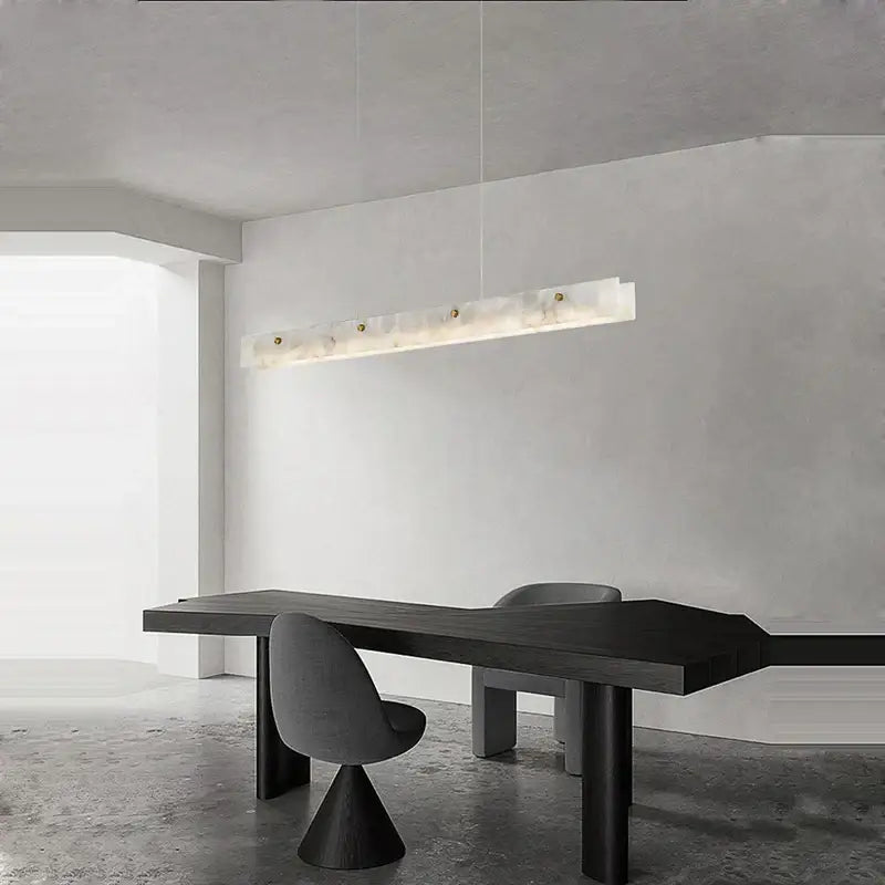 A modern art deco marble steel chandelier in black and gold featuring a sleek translucent white marble body above dining table
