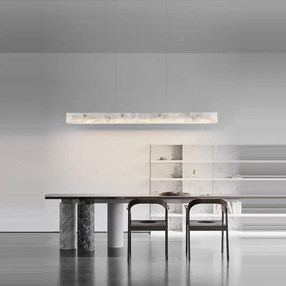A sleek rectangular pendant light with art deco marble white finish and gold-toned deco marble steel accents above dining table