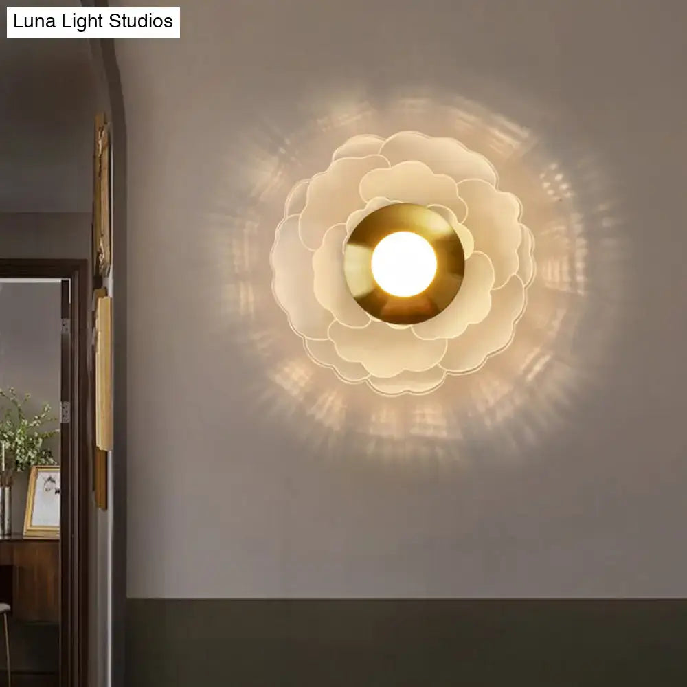 Modern art deco white and gold flower wall sconce light with layered glass and brass center emitting soft ambient light