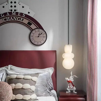 A white ceramic rabbit figurine in a red and black outfit stands on a dark wood nightstand under an alabaster indoor ceiling chandelier