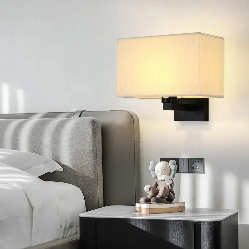 Modern beige and black elegant bedroom wall lamp featuring a rectangular fabric shade and black metal base wall lamp