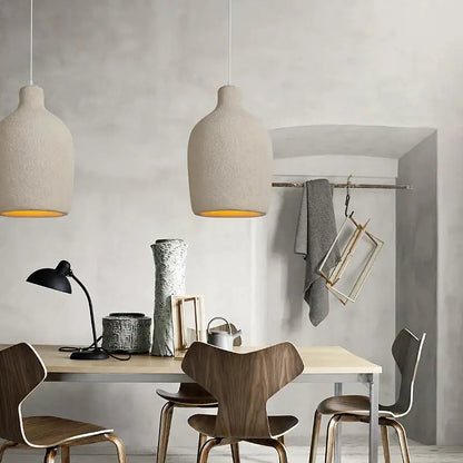 Two beige textured decorbites cement led chandelier pendant lights with warm yellow interiors hang above a dining table