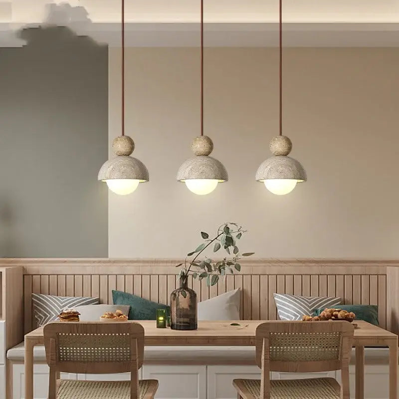 Three decorbites led pendant lights with matte concrete shades and warm cords hang above a wooden dining table
