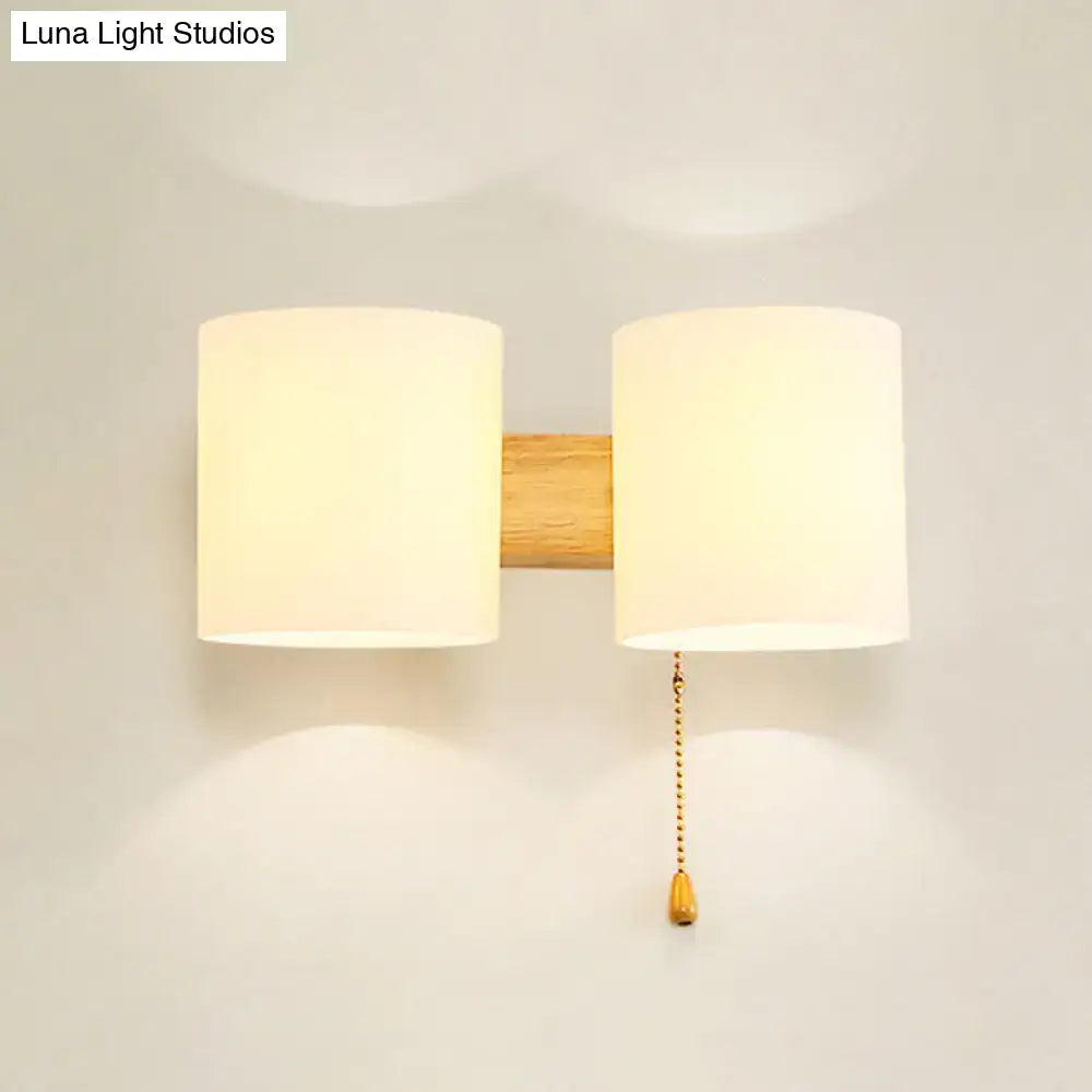 Minimalist modern beige fabric and wood wall light bedroom sconce with two shades and brass pull chain on wood bar