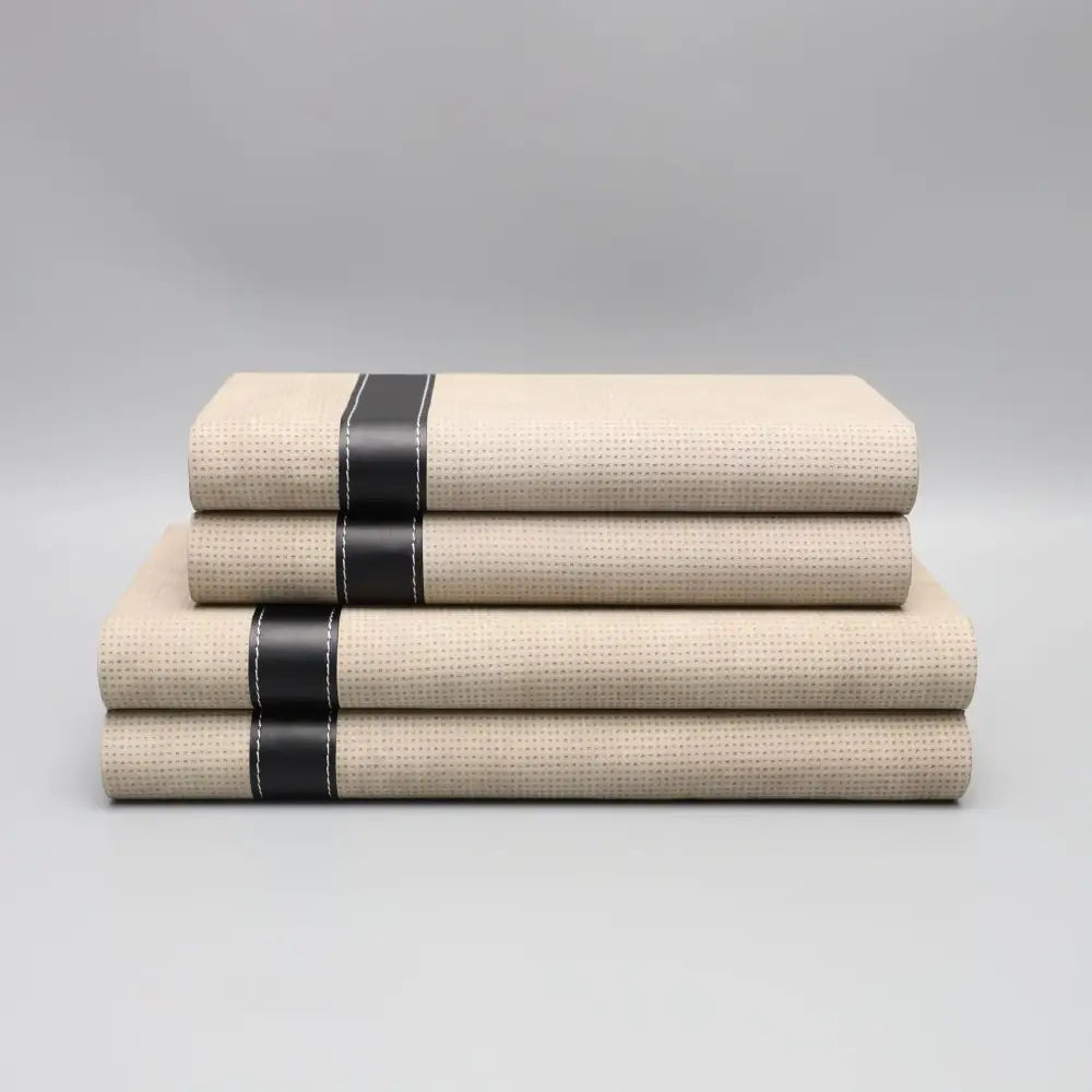 Stacked beige linen-like bed sheets with black leather straps and white stitching in modern beige geometric jewelry storage box decorbites