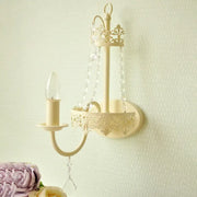 Beige ornate metal wall sconce with crystal chains and candle-style bulb 15 inch fixture for modern bedrooms