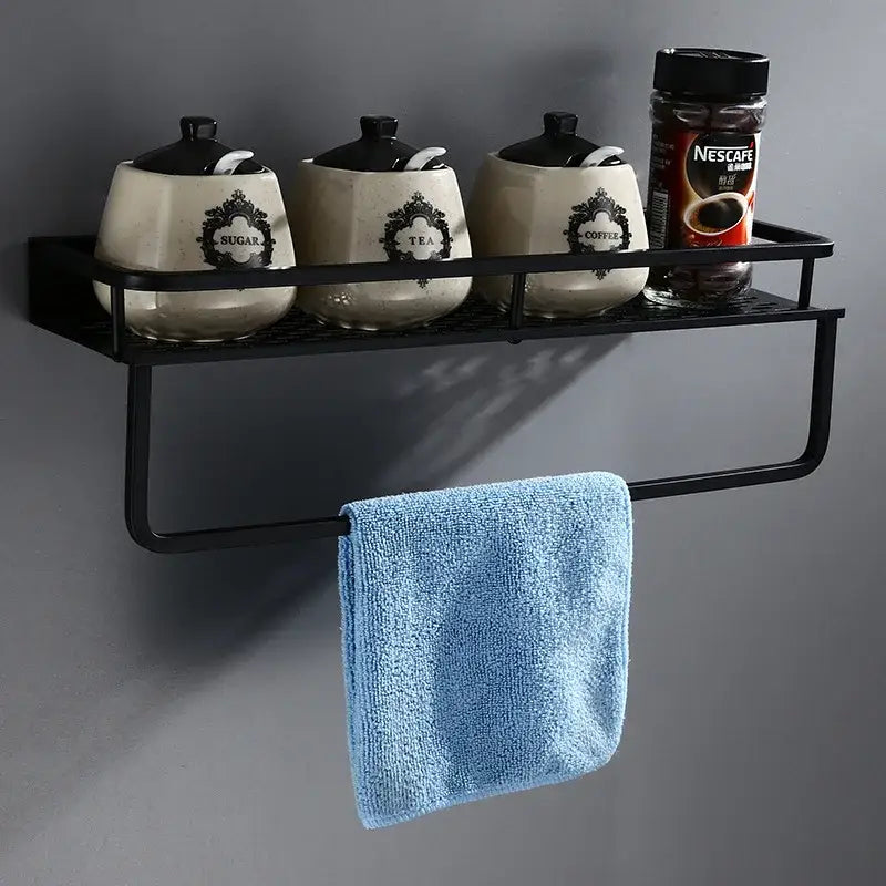 Modern black aluminum bathroom shelf with towel bar featuring wire mesh surface holding ceramic canisters and nescafe jar