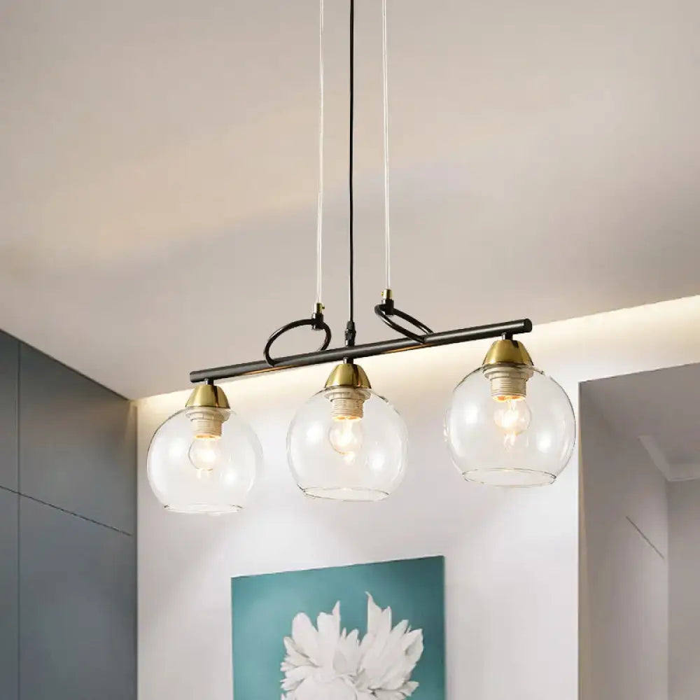 Modern black metal pendant light with three smoke gray glass globes and brass accents for dining hall island