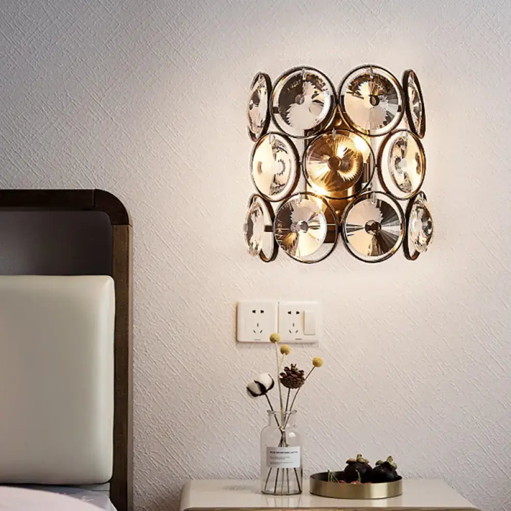 Modern black and brass wall mount light featuring clear crystal discs in an overlapping circular pattern for bedroom use